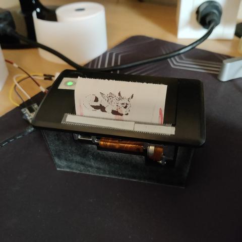 The thermal receipt printer which has a black and white image of Solstice the gryphon loafing printed out. Art by Blajn