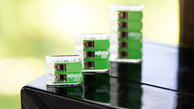 Promotional picture of several Wago 221 connectors with green levers, standing on a glossy black surface.