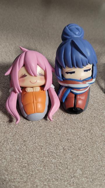 Mini figures of Nadeshiko and Rin from Yuru Camp. They're bundled up in sleeping bags with their eyes closed.