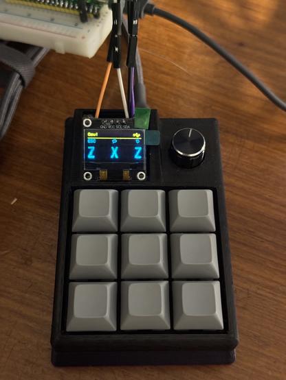 A DIY macropad with grey buttons, a screen and a rotary encoder. The screen shows “Osu!” in the top, as well three icons for esc, chat and restart. Below the icons there are three big letters, Z,X,Z which are the main keys to play Osu