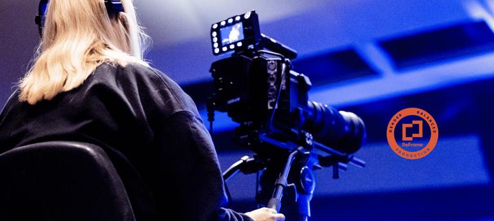 Image shows a female cinematographer at work in a blue lit studio. To the right is a circular red stamp showing the ReFrame logo. The words printed around the perimeter read: Gender Balanced Production.