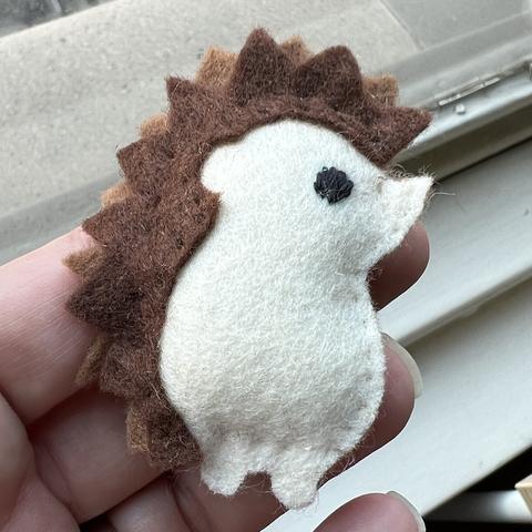 a cute fuzzy-felt hedgehog with a cream colored body and brown “spikes”