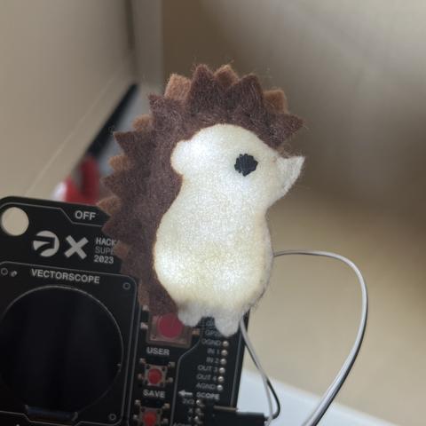 the fuzzy-felt hedgehog attached to a conference badge, with a glowing tummy (lit by internal LEDs)