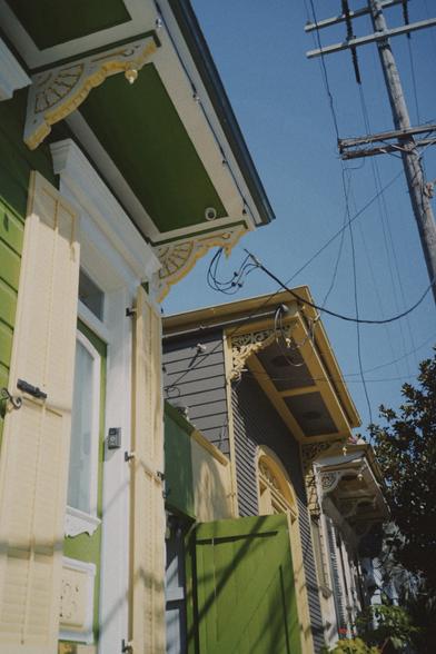 Hello angle shot of some New Orleans houses. One is green with white and cream framing and trim. The other is gray with a pale yellow trim.