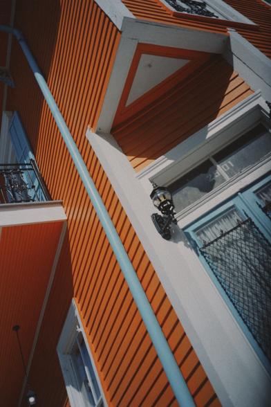 A Dutch angle of a New Orleans house. The house is two stories, bright orange and it has powder, blue doors, gutters, and window shutters.