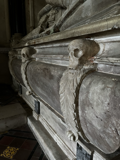 A closeup of the side of a grave monument, two skulls with a curved leaf motif underneath