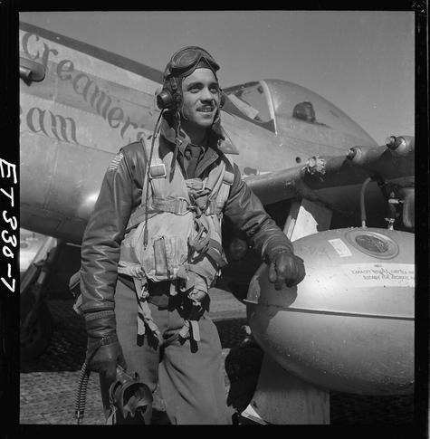 In this black and white photograph, we see a man standing next to an aircraft. The pilot is wearing full flight gear including a helmet with goggles attached on top of his head, earphones connected by wires going down the sides of his face into his ears, gloves which are visible on both hands gripping the wing of the plane in front him and strapped around his arms for added protection during flights; he also has boots on that seem to be high-topped or at least knee-length reaching above where most men's pants usually end. His uniform is what might have been worn by many service personnel from World War II, leather flying jackets with pockets all over which could hold numerous items needed in the cockpit such as maps, charts and other tools for navigation along with personal belongings like cigarettes.

On his jacket there are patches indicating rank or affiliation but we cannot make out exactly what they mean due to low resolution. He has a tool belt strapped around him probably containing various small tools essential during flight operations; possibly wrenches, screwdrivers etc., given the nature of such equipment being necessary in aviation maintenance and repair tasks.

The aircraft he is standing beside appears large with rounded front cockpit windows indicative of an older model plane - perhaps from World War II era. On its side we can see text which reads 'Creamer's Dream' suggesting it might be a name or nickname [...]