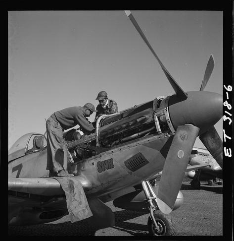 The image is a black and white photograph depicting two individuals working on the engine of an old military aircraft. The plane has visible markings, including the number "7" painted near its nose and the word "STAR" written vertically along one side.

One person appears to be wearing a pilot's uniform with patches or insignia indicative of rank or unit membership, while the other is dressed in casual clothing that could suggest they are not part of an official military crew. Both individuals seem focused on their task as they work together around the open engine bay of the aircraft. 

In the background, another similar type of plane can be seen parked on what looks to be a tarmac or airfield setting under clear skies. The overall scene gives off the impression that it was taken during World War II era when Tuskegee Airmen were active.

The photograph is credited as being part of a collection related to Marcellus G. Smith and Roscoe C. Brown, who are mentioned in the caption along with their respective home states - Louisville, Kentucky for Smith and New York, NY for Brown. Additionally, there's reference to an assignment or unit associated with Lowell Steward during March 1945 at Ramitelli, Italy.

The photo is labeled as "ET-3/8-6" in the bottom right corner along with a copyright symbol indicating it might be part of an archive collection by Tony Frissell.