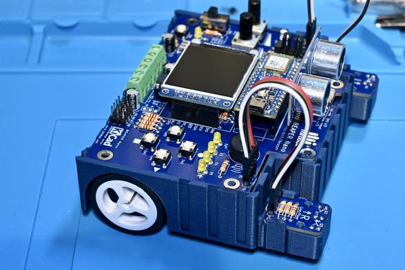A BEAPER Nano circuit controlled by an Arduino Nano ESP32 microcontroller is built as a rear-drive robot made using the BEAPER Bot design. The BEAPER Nano includes an on-board LCD display and SONAR distance sensor module, and its optical sensor modules have been mounted at the front of the BEAPER Bot chassis and connected with short extension cables.
