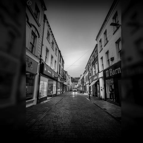 Monochrome vertical shot of empty retail street in town centre, with lights of a van in distance