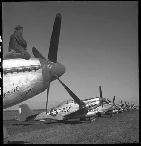 The image captures a historical moment featuring an unidentified Tuskegee airman seated on the wing of a World War II-era airplane, specifically a P-51 Mustang marked "Creamer's Dream." The man is dressed in period-appropriate military attire and wears sunglasses. In the background, several other similar airplanes are lined up on a dirt field under clear skies. This photograph appears to have been taken at Ramitelli Airfield in Italy during March 1945 as part of the Allied forces' operations against Axis powers. The black-and-white medium format nitrate film negative is from Tony Frissell's collection, indicating its significance and value as a historical record.