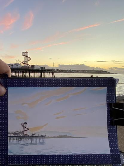 A yellowish blue Sunset with a pier with a slide, in front a watercolour of it.