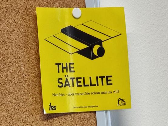 picture of sticker on a pinboard:

THE SÄTELLITE
Nett hier - aber waren Sie schon mal im All?
IRS Stuttgart logo
thesatellite.ksat-stuttgart.de
KSat logo
