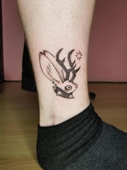 Photo of a tattoo I did of one of my "mini cryptids" flash designs. A lil jackalope head, with a large spiked collar on, and a soft little star/sparkle right in front of their antlers.