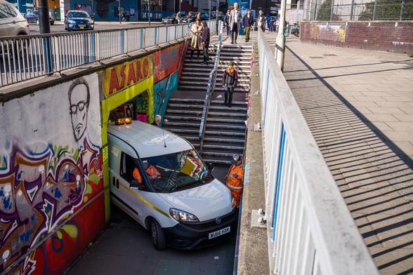 Photograph of stairs leading down to a pedestrian underpass. Emerging from the underpass is a van, with two workpeople in high-viz clothing. The van looks like it is stuck and can't get out from the underpass.