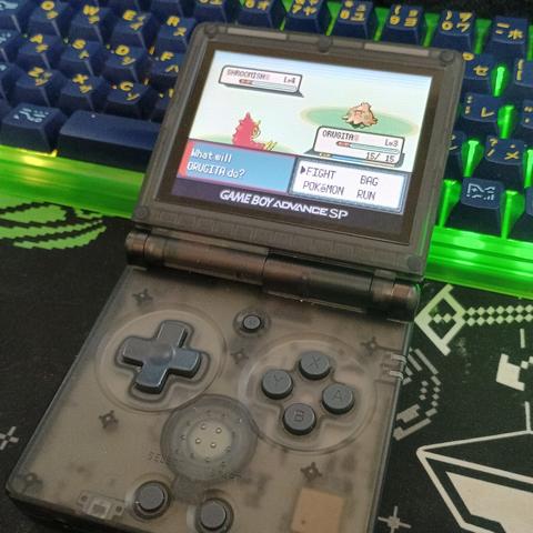 a photograph of a black transparent rg35xxsp playing pokemon emerald