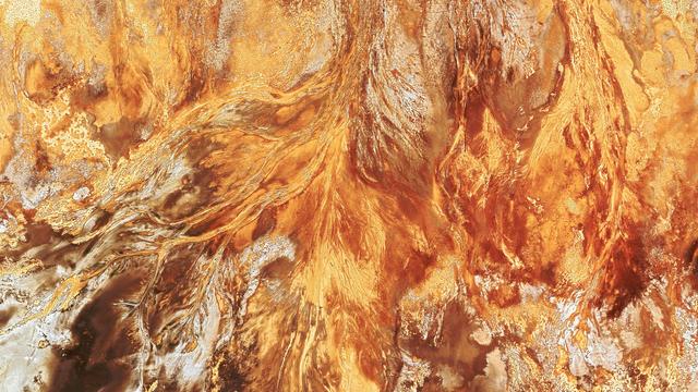 a desertic landscape seen from above, residual riverbeds form patterns that, combined with the yellow, orange and reds of the sand, look a bit like flames