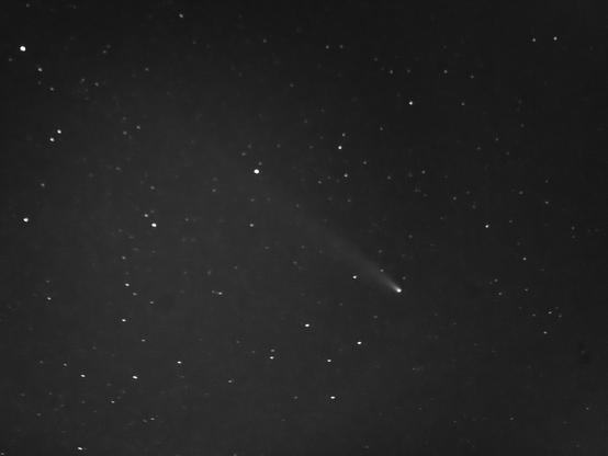 A black and white image of a night sky filled with stars, featuring a comet with a bright tail streaking across the top right area.

Czarno-biały obraz nocnego nieba wypełnionego gwiazdami, przedstawiający kometę z jasnym ogonem smugującym się w prawym górnym obszarze.