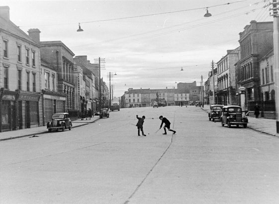 Two boys playing hurling in the middle of a very wide street in Thurles.
