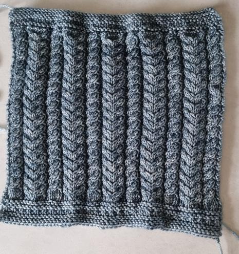 A 30cm knitted square. Hand-dyed yarn in a mid blue/grey.
The pattern is cables. 5 x 8 stitch plait cables between 6 x 4 stitch single cables