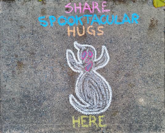 This image shows a chalk drawing on the sidewalk in front of our house. It consists of a (not very scary) ghost, and text that reads, "Share Sppoktacular Hugs Here"