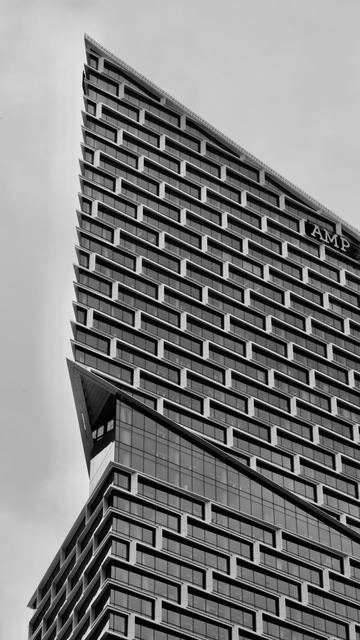Black and white photograph looking up at a tall office building.  The building has a regular pattern of rectangular windows on its angular sides.