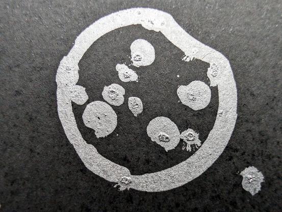 A minimalist desert scene under a moonlit sky, created using a pen plotter programmed to dip a paintbrush into silver metallic ink. The crescent moon floats above abstracted desert dunes and cacti, outlined in smooth lines. Scattered stars are represented with silver ink dabs, creating a serene, expansive night sky. The reflective quality of the silver ink against the black background evokes the calm and solitude of a desert night.  In close-up, the textured silver ink stars have a cratered, hand-painted appearance, adding dimension. The crescent moon is detailed with metallic strokes, enhancing the organic feel of the scene.  This piece meditates on the quiet of a desert night, its calm reinforced by each star and line being hand-programmed—each element unique, like every night spent under the sky.