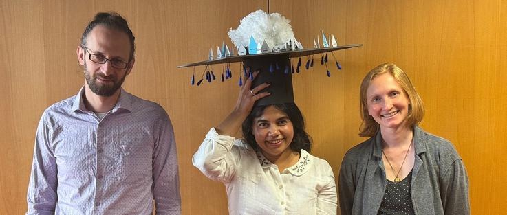 Shivani Sharma is surrounded by her two PhD advisors, wearing a hand-crafted PhD hat.