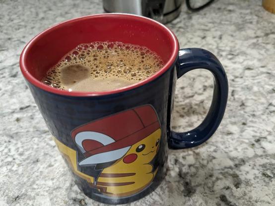 A Pikachu mug with coffee filling it.