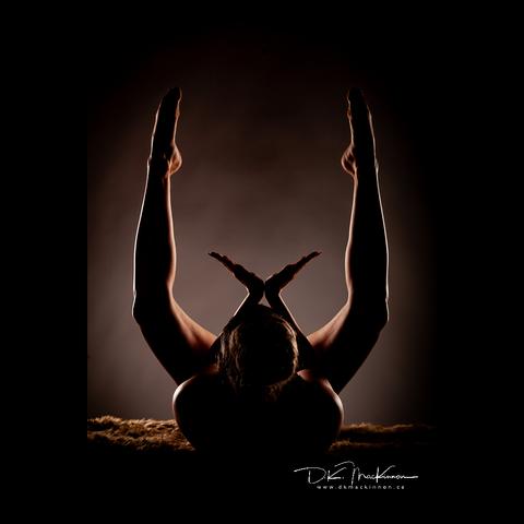A backlit woman on fur performing a yoga pose on her back, legs raised, hands together at the wrist and pointed outward.