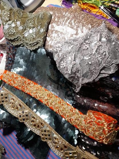 Scraps of fabric covered with sequins in different colours, valuable braids with gold embroidery on orange fabric and one with pearls, mirrors and gold. Large, fine lace.