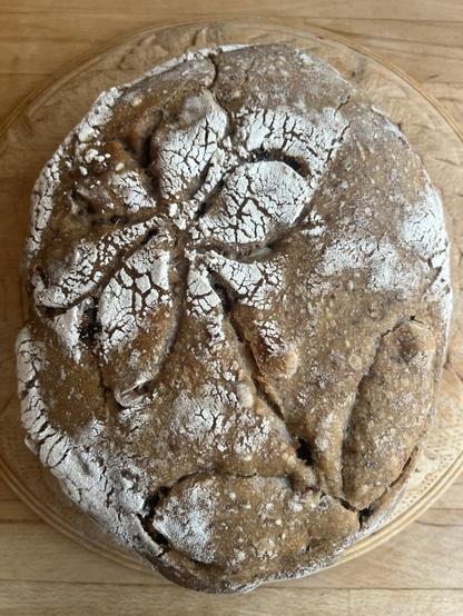 Finished, baked round loaf of bread with a traditional daisy type flower carved in the top, this time looking golden brown.