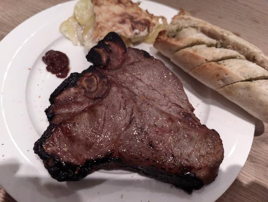 T-Bone-Steak mit Kartoffelgratin und Kräuterbaquette auf einem weißen Teller