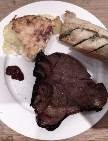 T-Bone-Steak mit Kartoffelgratin und Kräuterbaquette auf einem weißen Teller