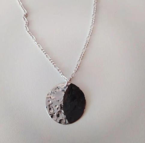 a moon shaped pendant with a silver chain. the "bright" side is glossy silver and the shaded oxidized dark silver
