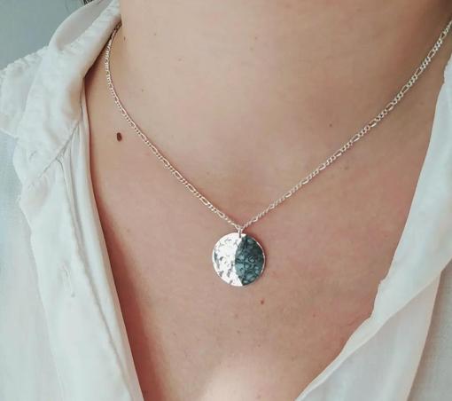 a moon shaped pendant with a silver chain. the "bright" side is glossy silver and the shaded oxidized dark silver. it's worn on woman's chest
