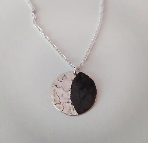 a moon shaped pendant with a silver chain. the "bright" side is glossy silver and the shaded oxidized dark silver