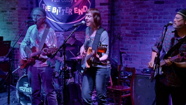 David Gans and the Broken Angels playing The Bitter End on Bleeker Street in Greenwich Village NYC on Thursday October 24, 2024. The band is playing on stage, which is in front of a brick wall and lit with purple, red & blue lights.
