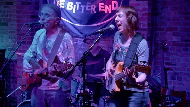 David Gans and the Broken Angels playing The Bitter End on Bleeker Street in Greenwich Village NYC on Thursday October 24, 2024. The band is playing on stage, which is in front of a brick wall and lit with purple, red & blue lights.
