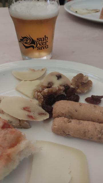 Cerveza del tipo "barricada" en el fondo, con un plato de quesos en primer plano.