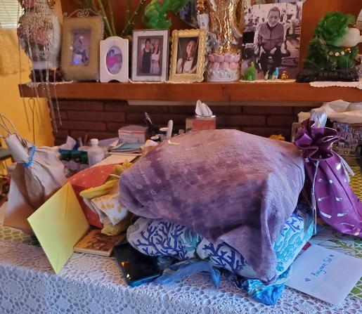 Birthday cards with birthday gifts on white crochet covered table with brick & wood mantle behind. The gifts are all wrapped in fabric & reused paper bags.