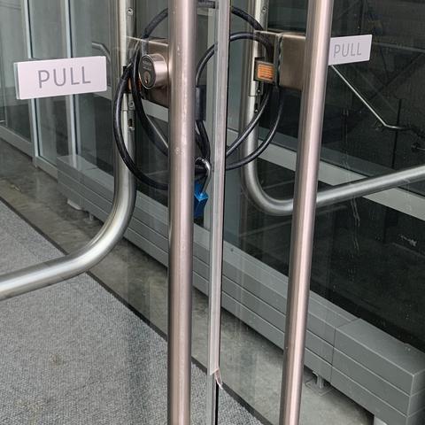 A pair of glass doors with elegant CRL exit devices are held internally by a bike cable lock. The doors also have PULL signs