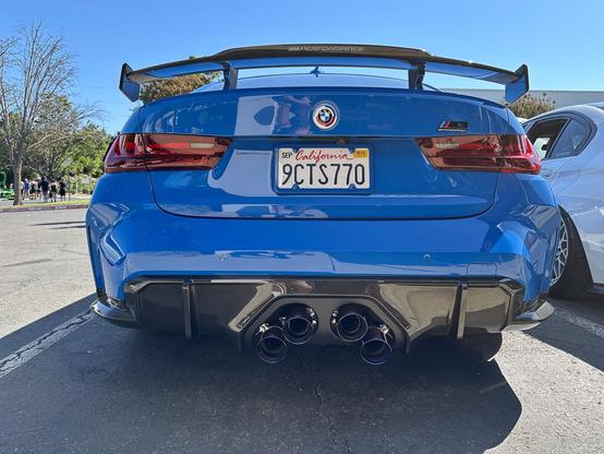 Rear end of blue sports sedan with found exhaust outlets arranged in a trapezoid shape.