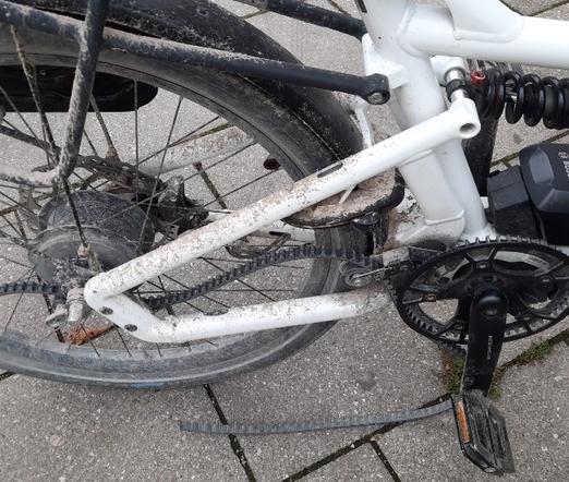 Gerissener Antriebsriemen eines weissen Lastenrades, das nach mehrfach täglicher  Fahrt über oben im Thread gezeigten Radweg entsprechend schlammverschmutzt ist.