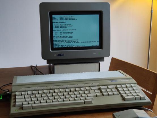 A front-on landscape photo of an Atari STFM on a wooden table, with a black-and-white high-resolution Atari SM124 monitor showing Termux's MOTD, indicating a successful login. Busybox's telnetd doesn't require any authentication: connect to the port, and you're in.