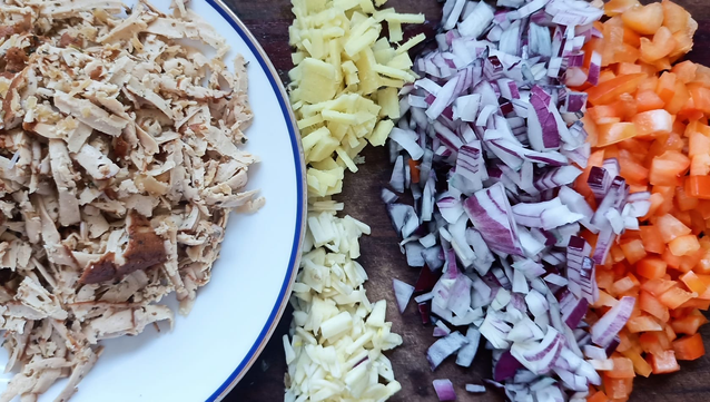 auf einem Brett geschnittene Zwiebel, Paprika, Ingwer Knoblauch + geriebener Tofu
