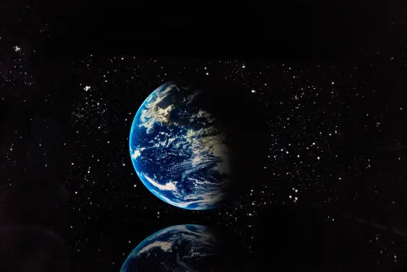 Picture of a video projection of an image of the earth, surrounded by stars. The image is reflecting in a water pool.