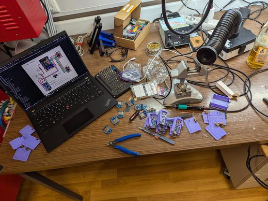 Messy soldering station. ThinkPad shows schematics, there's bunch of ESP8266, BMI160, 3D printed cases, lots of hot glue and tools