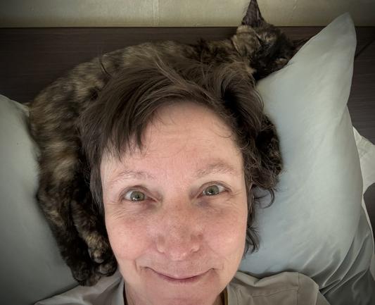 Indoors, bedroom. Selfie from my pillow with a slumbering tortoiseshell kitten draped over my head