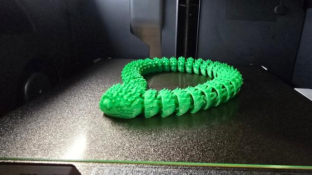 A 3D printed snake in a green colour on a print bed. All the parts are connected.